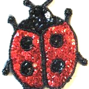 Peut inclure: Une coccinelle rouge et noire faite de paillettes. La coccinelle a des points noirs et une tête noire.