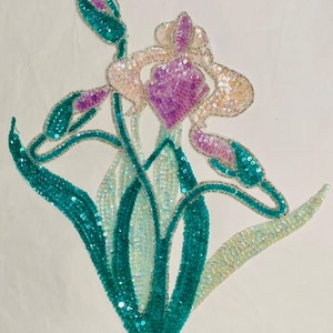 May include: A beaded applique of an iris flower with teal green leaves and pink and white petals.