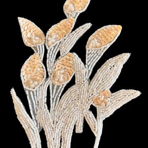 May include: A floral applique patch featuring a bouquet of stylized flowers crafted with iridescent champagne-colored sequins, small white seed beads, and elongated white bugle beads arranged in a vertical, layered botanical pattern.