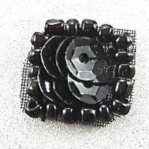 May include: A square black sequin and bead embellishment. The center features several black sequins, surrounded by small black beads. The embellishment is mounted on a black mesh backing, suitable for sewing or gluing onto fabric.