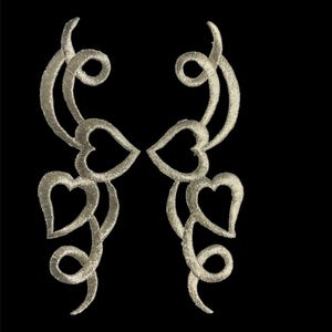 May include: Two silver embroidered patches with a swirling design and hearts. The patches are symmetrical and have a delicate, intricate design.