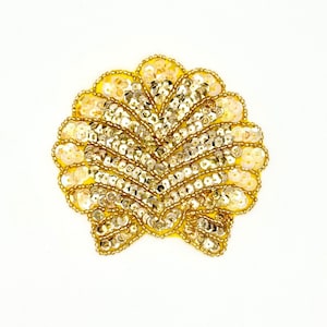 May include: A shell-shaped patch featuring a bright yellow fabric base adorned with rows of shimmering gold sequins and metallic gold beads. The design follows a fan-like pattern with scalloped edges, creating a textured and reflective surface.