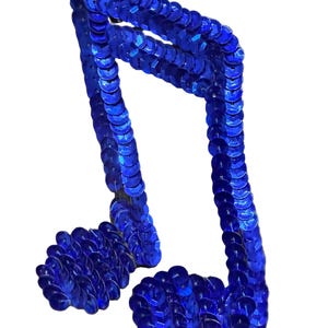 May include: A musical note applique covered in vibrant blue sequins. The design features two stems connected at the top, each ending in a rounded base, with the entire surface densely layered with small, reflective, circular blue sequins.
