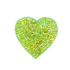 May include: A lime green heart-shaped patch, densely covered in shimmering sequins. The patch is outlined with small, light green beads. The sequins reflect light, creating a sparkling effect. The heart shape is symmetrical and centered.