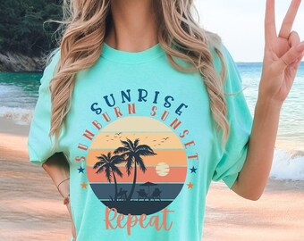 May include: A turquoise blue t-shirt with a graphic of a palm tree and sunset with the text "Sunrise Sunburn Sunset Repeat" in a circle.