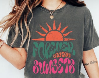 May include: A charcoal grey t-shirt with a graphic design of a sun with the text "FOREVER CHASING SUNSETS" in green and pink.