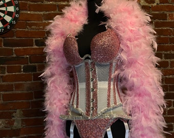 May include: A pink and white corset with a mesh overlay and rhinestone embellishments. The corset is on a mannequin with a pink feather boa.