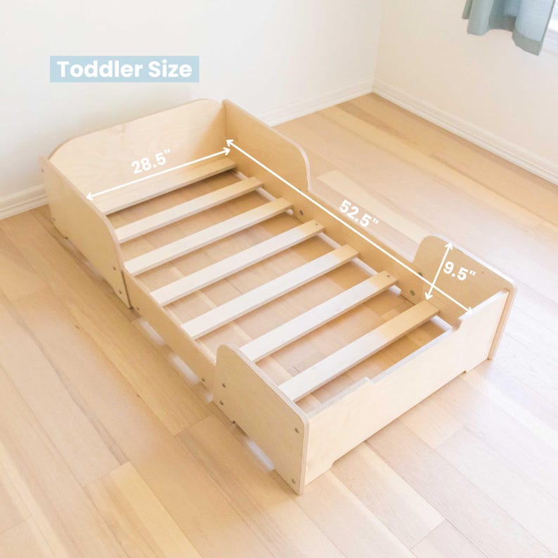 May include: A light-coloured wooden toddler bed with a slatted base. The bed frame has rounded corners and side rails. The bed measures 133.35 cm long, 72.39 cm wide, and 24.13 cm high. The text "Toddler Size" is in the image.