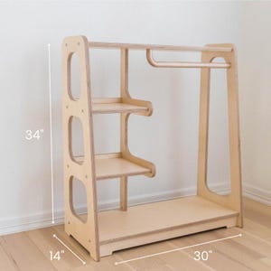 K&ouml;nnte beinhalten: Ein Kleiderst&auml;nder aus Holz mit drei Regalen und einer Kleiderstange. Der St&auml;nder ist 86 cm hoch, 76 cm breit und 36 cm tief.