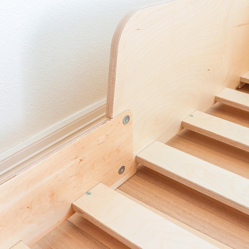 May include: Close-up of a wooden bed frame with a curved headboard. The frame is constructed from light-coloured wood, with visible grain. The bed slats are also made of wood. The frame is attached with metal screws.