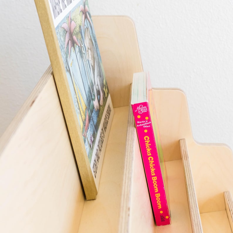 May include: A wooden bookshelf with five shelves, each holding a different book. The top shelf has a book titled "Where the Wild Things Are" and the bottom shelf has a book titled "Chicka Chicka Boom Boom".