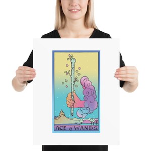 May include: A tarot card illustration of the Ace of Wands. The card features a hand holding a wand with a green sprout growing from the top. The background is a gradient of blue, yellow, and pink with clouds and a mountain in the distance.