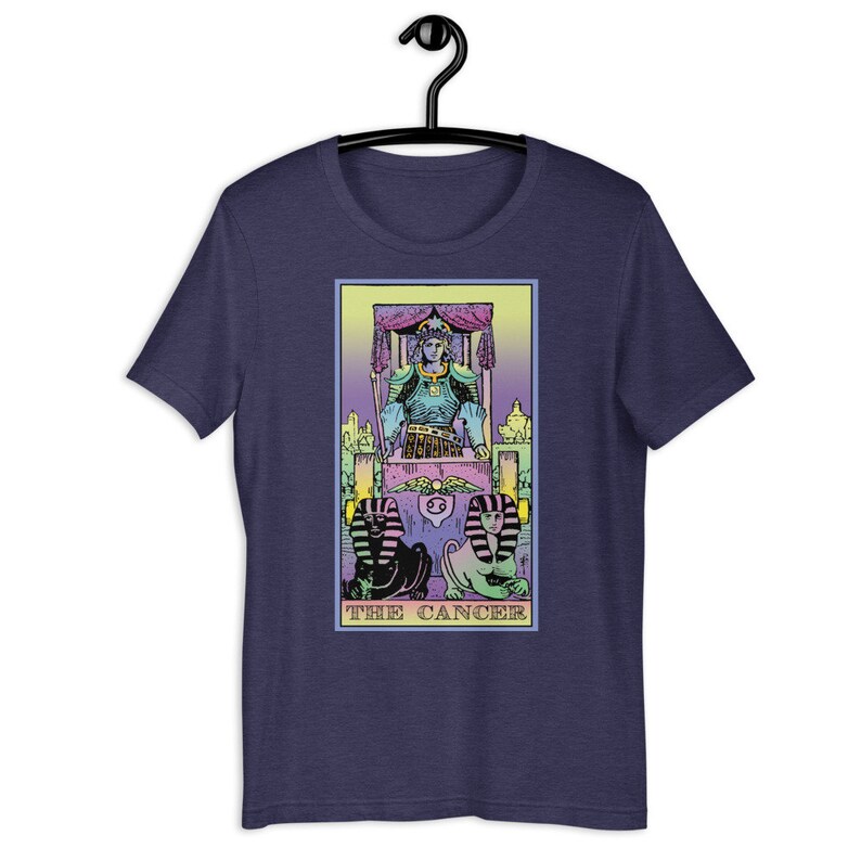 Puede incluir: Una camiseta azul marino con una ilustraci&oacute;n en colores pastel de la carta del tarot El C&aacute;ncer. La carta presenta una figura sentada en un trono con dos figuras de esfinge en la parte inferior.