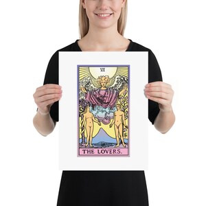 May include: The Lovers tarot card, featuring a winged angel above two nude figures standing on either side of a mountain. The card is framed in a white border and has a pink and purple gradient background.