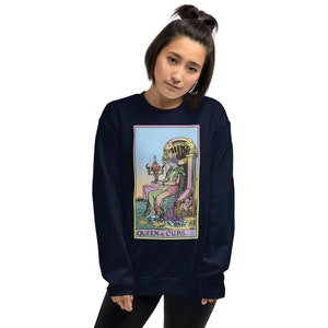 Puede incluir: Sudadera azul marino con una ilustraci&oacute;n colorida de la carta del tarot de la Reina de Copas. La carta representa a una mujer sentada en un trono con una copa en la mano. El texto "QUEEN of CUPS." est&aacute; impreso debajo de la carta.