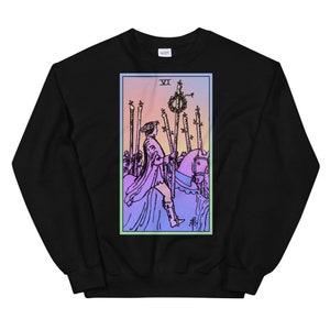 May include: Black sweatshirt with a colorful illustration of the Six of Wands tarot card. The card features a knight riding a horse, holding a staff with a wreath on top. The card is surrounded by a light blue border.