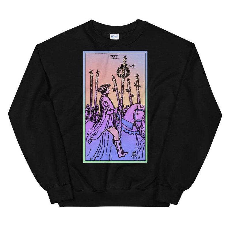 May include: Black sweatshirt with a colorful illustration of the Six of Wands tarot card. The card features a knight riding a horse, holding a staff with a wreath on top. The card is surrounded by a light blue border.