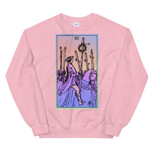 May include: Pink sweatshirt with a colorful illustration of the Six of Wands tarot card. The card features a rider on horseback, holding a staff with a wreath on top. The card is surrounded by a light blue, green, and pink border.