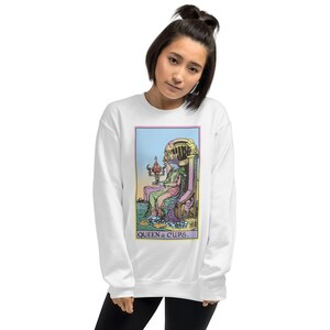 Puede incluir: Sudadera blanca con una ilustraci&oacute;n colorida de la carta del tarot de la Reina de Copas. La carta muestra a una mujer sentada en un trono con una copa en la mano. El texto "QUEEN of CUPS." est&aacute; impreso debajo de la imagen.