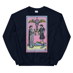 May include: Navy blue sweatshirt with a colorful illustration of the Two of Cups tarot card. The card features two figures holding cups, a winged serpent, and the Roman numeral II.
