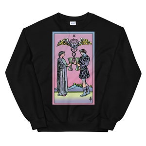 May include: Black sweatshirt with a colorful illustration of the Two of Cups tarot card. The card features two figures holding cups, a winged serpent, and the Roman numeral II.