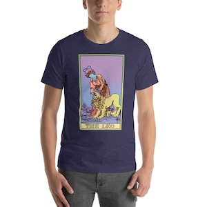 May include: A navy blue t-shirt with a graphic of the The Leo tarot card. The card features a person with a halo and a lion. The card is surrounded by a pink, purple, and yellow gradient.