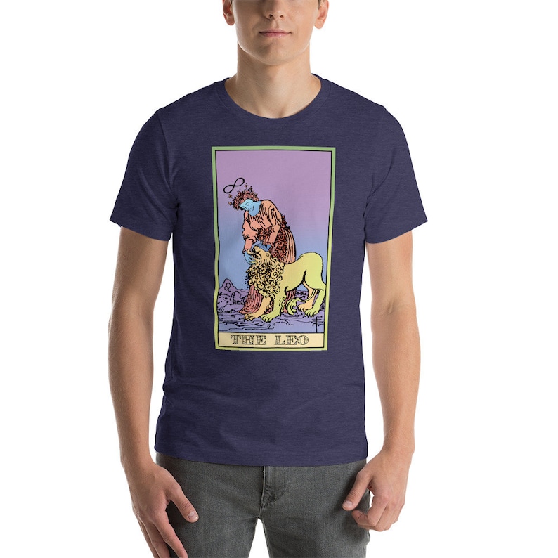 May include: A navy blue t-shirt with a graphic of the The Leo tarot card. The card features a person with a halo and a lion. The card is surrounded by a pink, purple, and yellow gradient.