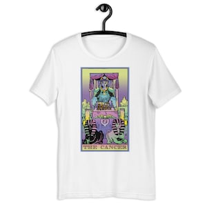 Puede incluir: Camiseta blanca con una ilustraci&oacute;n colorida de una carta de tarot, El C&aacute;ncer. La carta presenta una figura en un trono con dos figuras arrodilladas en la parte inferior.