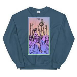 May include: A blue sweatshirt with a pastel pink and blue gradient background featuring a tarot card illustration of the Six of Wands. The card depicts a rider on horseback holding a staff, with five other staffs standing upright in the background. The card number "VI" is visible in the top left corner.