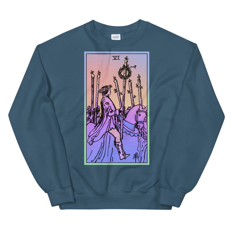 May include: A blue sweatshirt with a pastel pink and blue gradient background featuring a tarot card illustration of the Six of Wands. The card depicts a rider on horseback holding a staff, with five other staffs standing upright in the background. The card number "VI" is visible in the top left corner.