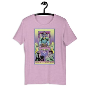 Puede incluir: Una camiseta rosa con un dise&ntilde;o de carta de tarot en colores pastel que presenta una figura sentada en un trono con dos figuras de esfinge en la parte inferior. La carta dice "THE CANCER".