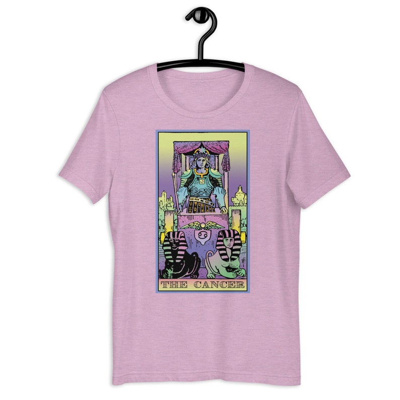 Puede incluir: Una camiseta rosa con un dise&ntilde;o de carta de tarot en colores pastel que presenta una figura sentada en un trono con dos figuras de esfinge en la parte inferior. La carta dice "THE CANCER".