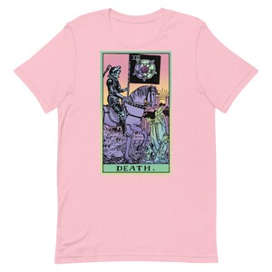 Puede incluir: Camiseta rosa claro con un dise&ntilde;o de carta del tarot. La carta representa una figura esquel&eacute;tica a caballo, sosteniendo una bandera con una rosa. La palabra "DEATH" est&aacute; impresa en la parte inferior de la carta en un marco verde.
