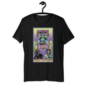 Puede incluir: Camiseta negra con una ilustraci&oacute;n colorida de la carta del tarot El C&aacute;ncer. La carta presenta una figura con una corona sentada en un trono con dos figuras de esfinge en la parte inferior. El texto "THE CANCER" est&aacute; impreso debajo de la imagen.