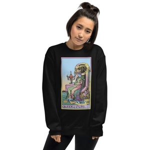 Puede incluir: Sudadera negra con una ilustraci&oacute;n colorida de la carta del tarot de la Reina de Copas. La carta representa a una mujer sentada en un trono con una copa en la mano. El texto "QUEEN of CUPS." est&aacute; impreso debajo de la carta.