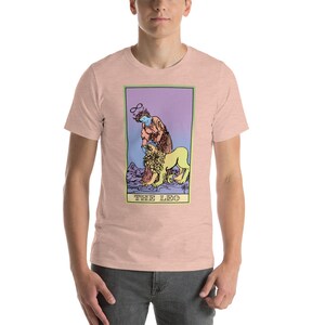 May include: A pink t-shirt with a colorful illustration of the tarot card "The Leo". The card features a person with a halo and a lion.