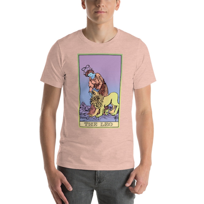 May include: A pink t-shirt with a colorful illustration of the tarot card "The Leo". The card features a person with a halo and a lion.