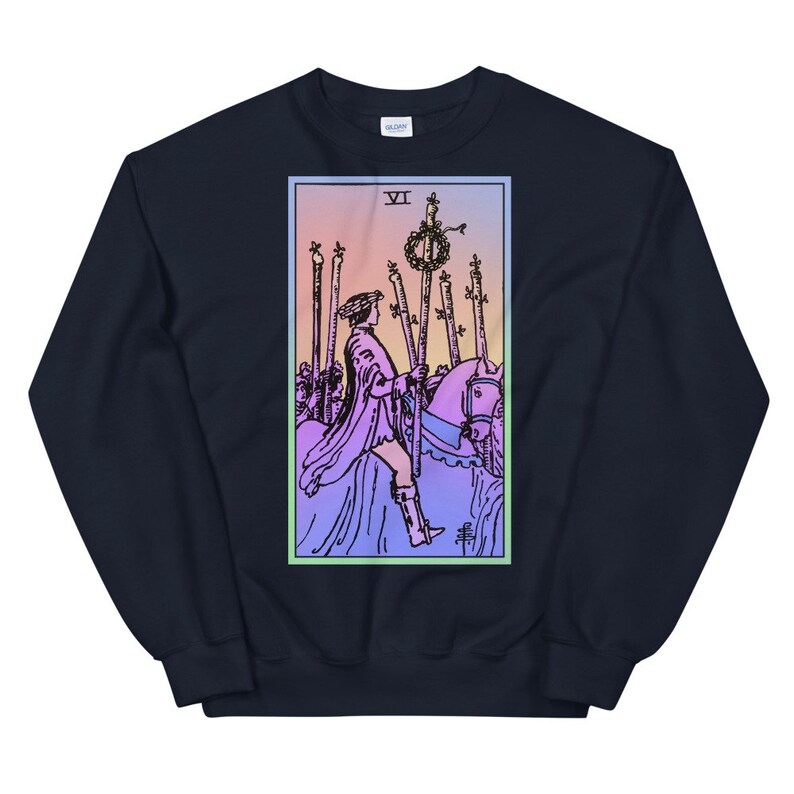 May include: A navy blue sweatshirt with a colorful illustration of the Six of Wands tarot card. The card features a rider on horseback, holding a staff with a wreath on top, surrounded by five other staffs.