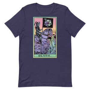 Puede incluir: Camiseta azul marino con un dise&ntilde;o de carta del tarot. El gr&aacute;fico representa una figura esquel&eacute;tica a caballo, sosteniendo una bandera con una rosa. La palabra "DEATH" est&aacute; impresa debajo. El dise&ntilde;o est&aacute; en un marco rectangular.