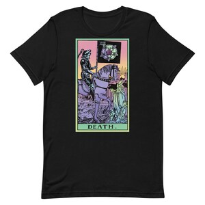 Puede incluir: Camiseta negra con un dise&ntilde;o de carta del tarot. El gr&aacute;fico representa una figura esquel&eacute;tica a caballo, sosteniendo una bandera con una rosa, con la palabra "DEATH" en la parte inferior. El dise&ntilde;o tiene una est&eacute;tica vintage y colorida.