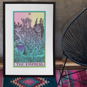 May include: A framed print of The Empress tarot card. The artwork features a seated figure with a crown, holding a scepter, in a colorful, pastel-toned design. The card's title, "THE EMPRESS," is printed at the bottom. The frame is black.