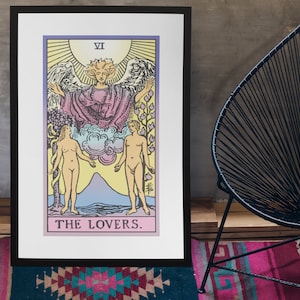 May include: A framed tarot card print depicting The Lovers card from the Rider-Waite tarot deck. The card features a winged angel above two nude figures standing on either side of a mountain. The card is titled "THE LOVERS."