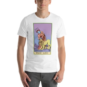 May include: White t-shirt with a colorful illustration of a tarot card, The Leo, featuring a person with a halo and a lion. The card has a purple, pink, and green gradient background.