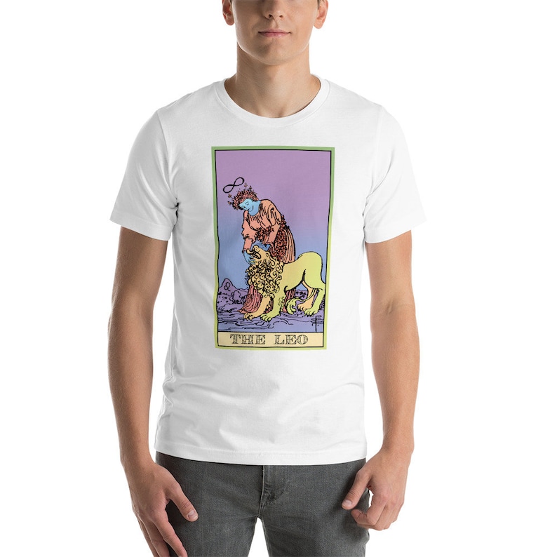 May include: White t-shirt with a colorful illustration of a tarot card, The Leo, featuring a person with a halo and a lion. The card has a purple, pink, and green gradient background.