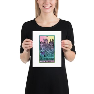 May include: A framed print of The Empress tarot card. The artwork features a seated figure in a flowing gown, with a crown and scepter. The card has a colorful design with a green, pink, and blue color scheme. The text "THE EMPRESS" is at the bottom.