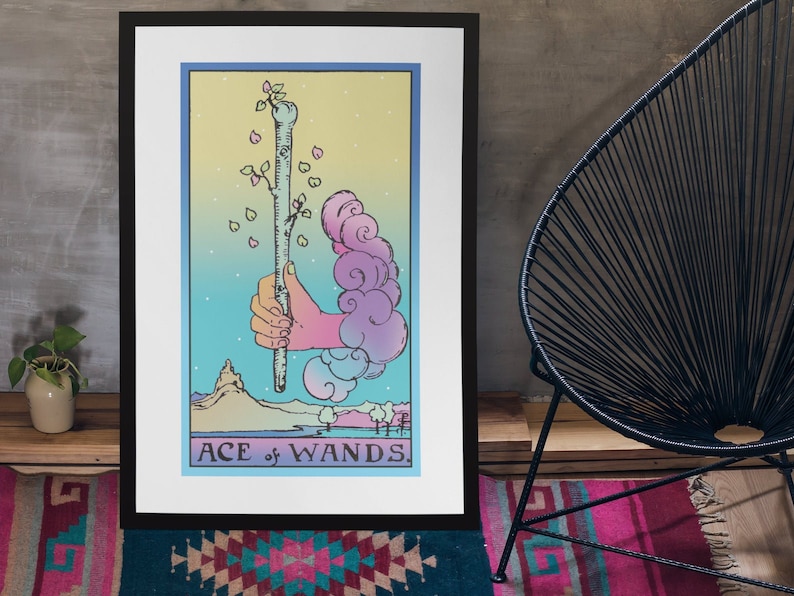 May include: A framed print of the Ace of Wands tarot card. The card features a hand holding a wand with a green sprout growing from the top. The background is a gradient of blue, pink, and yellow with clouds and a mountain in the distance. The text "ACE of WANDS" is printed at the bottom of the card.