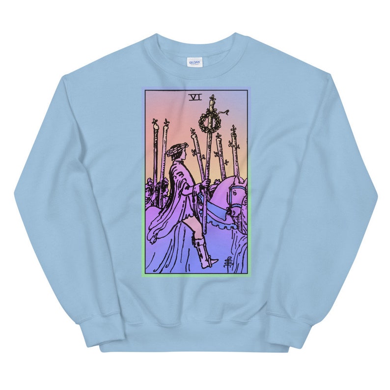 May include: Light blue sweatshirt with a graphic print of the Six of Wands tarot card. The card features a rider on horseback with a staff in hand, surrounded by other staffs. The background is a gradient of pink, orange, and yellow.