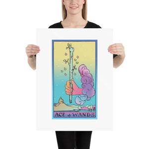 May include: A tarot card illustration of the Ace of Wands. The card features a hand holding a green wand with a small tree growing from the top. The background is a gradient of blue, yellow, and pink with clouds and a mountain in the distance. The text "ACE of WANDS" is printed at the bottom of the card.