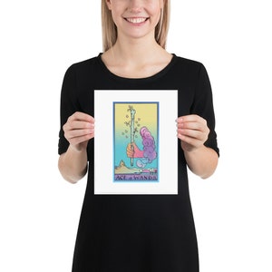 May include: A tarot card print featuring the Ace of Wands. The card depicts a hand holding a wand with leaves growing from it. The background is a colorful gradient of blue, yellow, and pink.