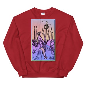 May include: Red sweatshirt with a graphic of the Six of Wands tarot card. The card features a rider on horseback with a crown of laurels and a staff. The card is surrounded by a blue and green border.